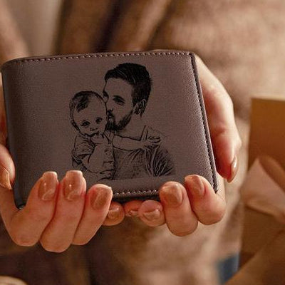 Person holding a gray wallet with an engraved image of a man and child.